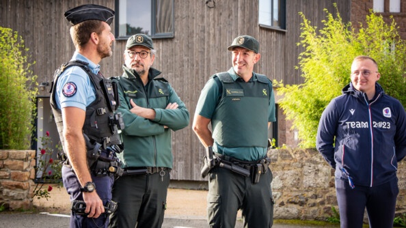 De gauche à droite, échageant, un gendarme français de profil droit, deux membres de la Guardia civil (le premier les bras croisés, le second les bras dans le dos), et un civil en tenue de sport, les bras dans le dos, portant une veste bleue marine siglée (team 2023)