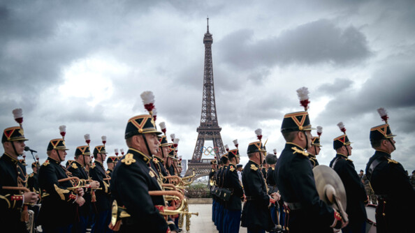 photo de la Tour Eiffel revêtant les anneaux olympiques. Devant elle, de biais, se tiennent des gardes républicains.