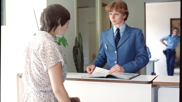 Une femme gendarme accueille à la banque d'accueil d'une brigade de gendarmerie une femme de dos avec son enfant