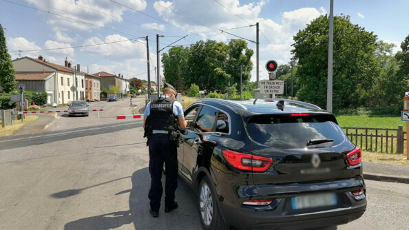 Un gendarme, vu de dos, dispense des conseils de pr&eacute;vention au conducteur d'un v&eacute;hicule noir arr&ecirc;t&eacute; &agrave; un passage &agrave; niveau, dont les barri&egrave;res sont baiss&eacute;es. Au second plan, un second v&eacute;hicule est arr&ecirc;t&eacute; de l'autre c&ocirc;t&eacute; du passage &agrave; niveau.