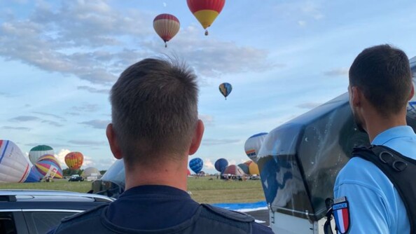 Un polizei allemand et un gendarme français de l'UOFA vus de dos, observant les abords de l'aérodrome, d'où décollent des montgolfières.