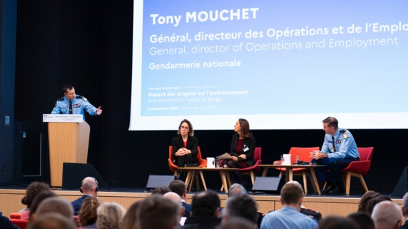 Photo du g&eacute;n&eacute;ral Tony Mouchet qui intervient lors d'un colloque. Le militaire s'exprime au micro devant l'assembl&eacute;e, debout derri&egrave;re un pupitre en bois.