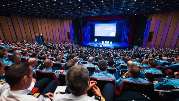 Vue plongeante sur un amphithéâtre rempli d'officiers de gendarmerie vus de dos. En arrière plan, sur scène, le directeur général