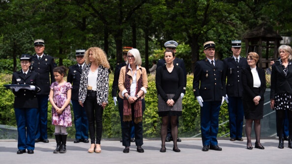 Lors d'une cérémonie officielle, des civils sont entourés de militaires. Tous se tiennent debout, dans un espace extérieur et verdoyant.