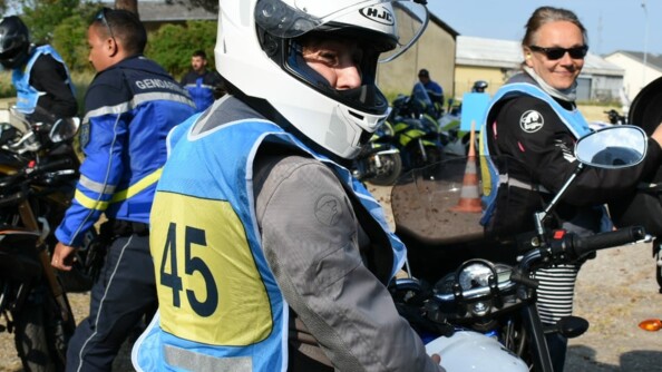 Motocycliste civil casqu&eacute;, portant un dossard bleu et jaune num&eacute;rot&eacute; 45, &agrave; cheval sur sa moto. En arri&egrave;re-plan, &agrave; droite, une autre motocycliste, non casqu&eacute;e, et &agrave; gauche, un motocycliste de l'EDSR 78 de trois-quart dos.