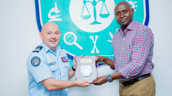 A gauche, le colonel de gendarmerie Laurent Lesaffre, en tenue, au côté d'un représentant du laboratoire médico-légal du Rwanda en civil (à droite). Les deux hommes, tenant une plaque de remerciements, posent devant un panneau représentant le logo du laboratoire.