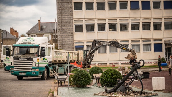 Photo d'un  b&acirc;timennt en b&eacute;ton beige et en pierres grises, devant lequel est stationn&eacute; un camion de chantier. une ancre marine appara&icirc; sur un terre-plein central