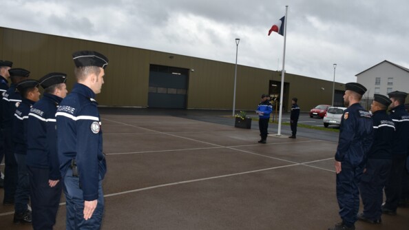 Gendarmes au garde-à-vous sur une place d'armes pendant qu'un officier face à eux lit l'ordre du jour.