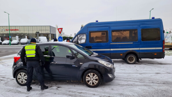 Des gendarmes contrôlent un véhicule bleu foncé. en arrière plan la ville et un camion de gendarmerie mobile