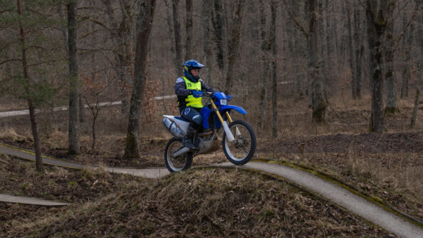 Une motarde de la gendarmerie sur une moto cross roule sur une étroite bande de goudron dans la forêt aux couleurs rousses