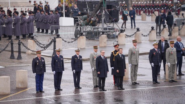 Deux hommes en civil devant des autorités militaires alignées devant un rond point