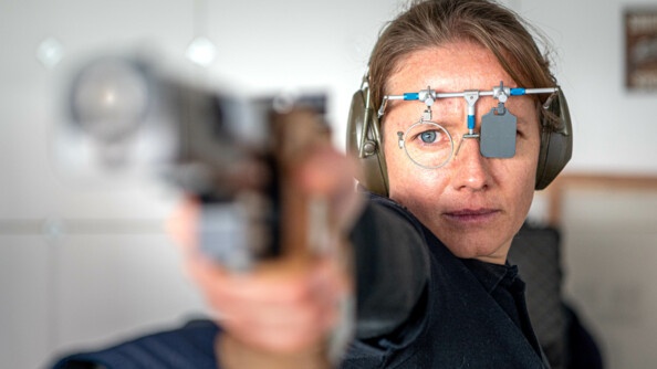 Gaelle Edon, de face avec un casque sur les oreilles, des luenttes de tir pointant son pistolet vers la cible.