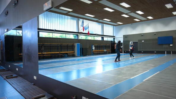Dans le reflet du miroir mural, deux escrimeurs s'affrontent dans une salle d'armes