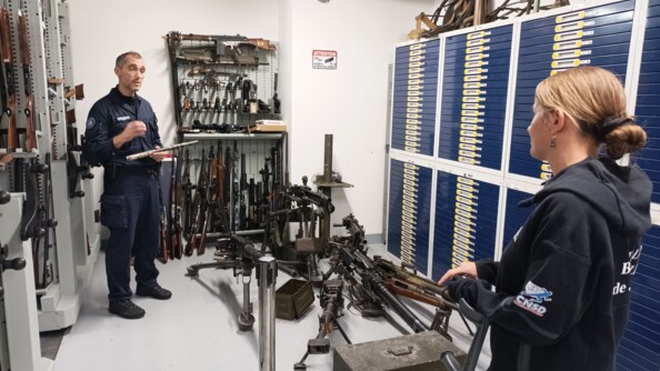 La para-sportive Gaëlle Edon, Sportive de haut-niveau de la Défense - Gendarmerie (SHND-G), de dos à droite, disctute avec un expert en ballistique de l'Institut de recherche criminelle de la gendarmerie nationale. Autour d'eux de nombreuses armes à feu.