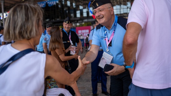 Le directeur général de la gendarmerie nationale, présent au Club France, serre la main d'une femme, que l'on aperçoit de dos. Plusieurs personnes se trouvent autour d'eux.