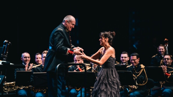 un colonel de la musique de la garde republicaine et une femme en logue robe grise se serrent les mains en souriant, devant les musiciens de la garde