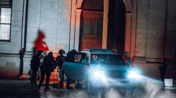 Le blindé phares allumés de l'AGIGN de nuit, devant une grande porte du château de Chambord avec des opérateurs autour dans l'ombre
