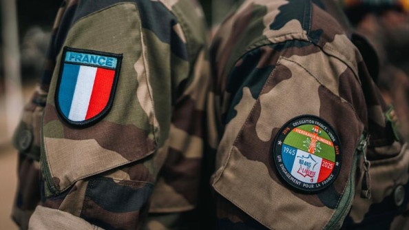 deux bras, revêtues d'une chemise kakie, sont appuyés l'un contre l'autre. l'un porte un écusson représentant le drapeau français. l'autre un écusson sur leqeul est inscrit "Délégation française - Un engagement pour la France - 1945 - 2025"