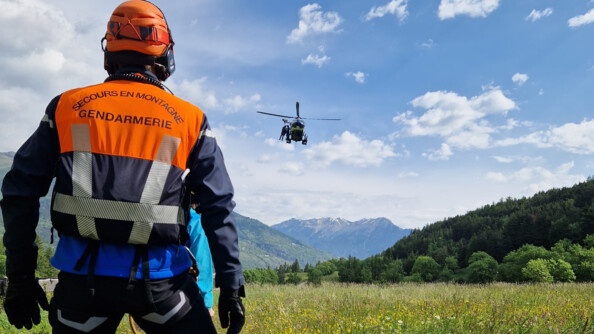 Un gendarme de PGHM attend le treuillage d'un hélicoptère au-dessus de la vallée. Deux hommes apprêtent à descendre