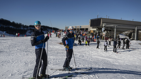 Deux gendarmes sur des skis devant une station enneigée et la foule de skieurs sous un ciel bleu
