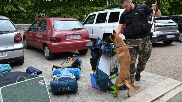 La photo représente un gendarme, accompagné d'un berger belge malinois, reniflant un sac contre lequel il est dressé, à l'occasion du festival Garorock