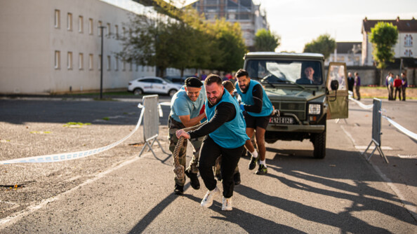 4 personnes portant une chasuble bleu ciel tirant un véhicule militaire avec une corde en riant