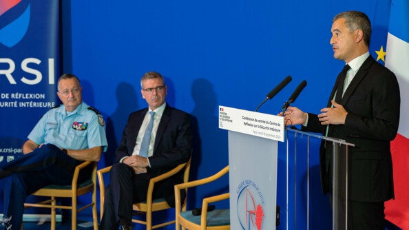 A droit, le minsitre de l'intérieur et des outre-mer, Gerald Darmanin, s'exprime derrière un pupitre pour la conférence de rentrée du Centre de réflexion sur la sécurité intérieure (CRSI). A gauche de l'image, assis sur des chaises et le regardant, un homme en costard et le Directeur général de la gendarmerie nationale