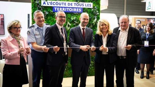 Dans le batiment où se tient le salon des Maires porte de Versailles à Paris, six personnes dont le directeur général de la gendarmerie et la ministre déléguée chargée des Collectivités territoriales et de la Ruralité coupent un ruban.