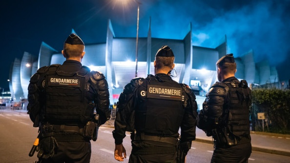 Trois gendarmes mobiles de dos au pied d'un stade éclairé