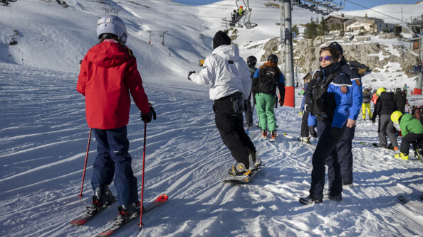 Deux gendarmes sur la droite, devant des skieurs et snow-boarder, dans la neige, aux pieds des remontées mécaniques