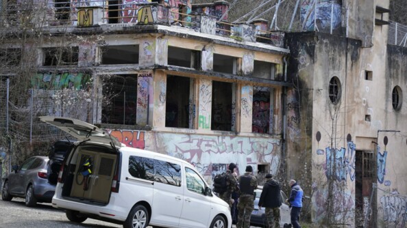 des gendarmes en bleu et un treillis devant des bâtiments tagués et anciennement brûlés