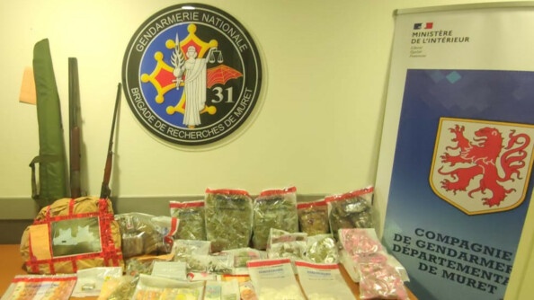 Saisies de cannabis (herbe et résine), liquide, armes et gilets pare-balles sur une table, le tout sous scellé. A droite un kakémono de la compagnie de gendarmerie départementale de Muret. AU mur, au-dessus de la saisie, l'écusson grand format de la Brigade de recherches de Muret