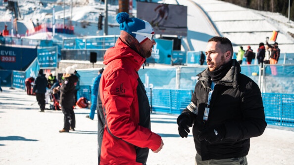 Le TSLO, un gendarme mobile habillé en civil avec un brassard gendarmerie est entrain de parler à un membre d'une délégation étrangère devant la grande piste de Courchevel. Cela, à l'occasion des championnats du monde de Courchevel.