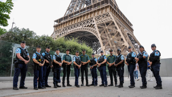 Un groupe de gendarmes français, entourés de trois membres de la Guardia civile, se tiennent debout, côte à côte, devant la Tour Eiffel.