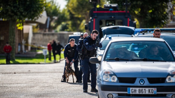 Démonstration d'interpellation: deux hommes deux une clio grise, mains sur la tête, en arrière un gendarme en combinaison bleu marine prend une visée avec une arme d'épaule et ses équipiers sont derrière lui, avec un chien