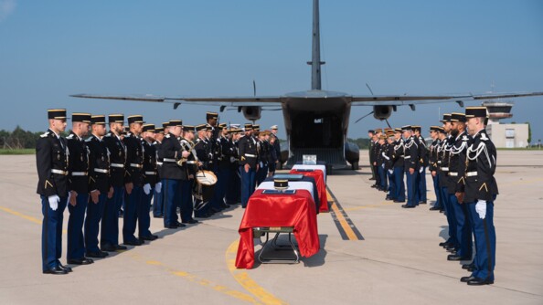De part et d'autre de deux cercueils recouverts du drapeau français, une vingtaine de gendarmes et autorités civiles et militaires sont au garde-à-vous sur le tarmac. En arière plan, l'avion qui vient de les déposer