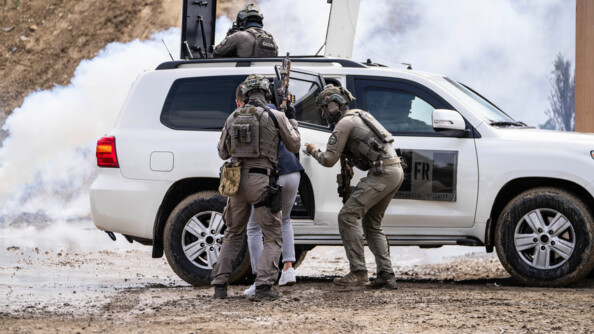 Un bin&ocirc;me du GIGN en protection d'un civil qu'ils font monter &agrave; bord d'un 4x4 blanc. Du toit ouvrant sort un militaire arm&eacute; en protection