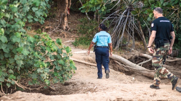 Une réserviste marche de dos sur un sentier suivie par un gendarme en treillis.