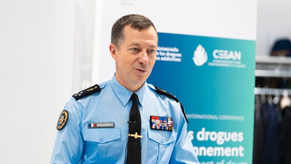 Photo du g&eacute;n&eacute;ral Tony Mouchet, posant devant l'affiche du colloque