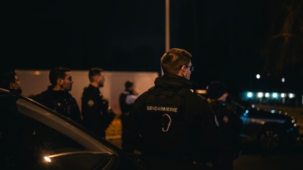 Vue de dos de plusieurs gendarmes qui regardent vers la droite de l'image. Il fait nuit et sombre.