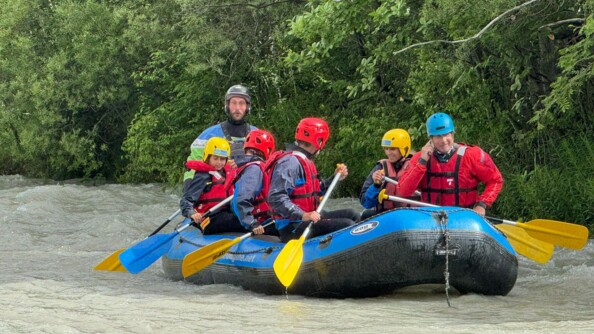 Six personnes sur un bateau et dans l'eau, en train de ramer, lors d'une session de rafting.