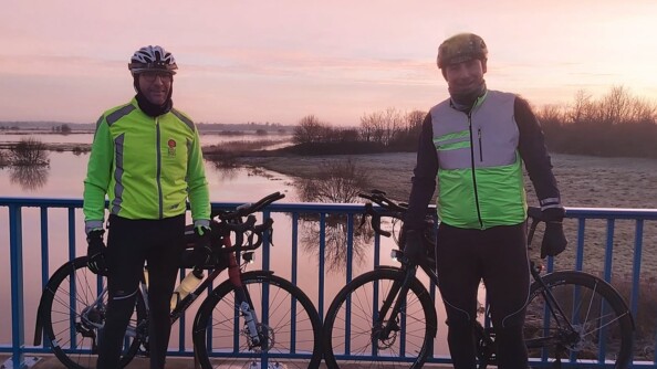 Photo des deux gendarmes lors d'un entraînement de 200km. A droite le gendarme Jérémie et à gauche l'adjudant Frédéric. Ils se trouvent tous les deux un pont, devant leurs vélos. Dans le fond, on aperçoit de l'herbe ainsi qu'une étendue d'eau.