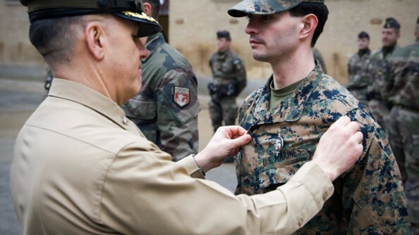 Un officier des Marines tend la veste de son subordonné  qui porte un brevet