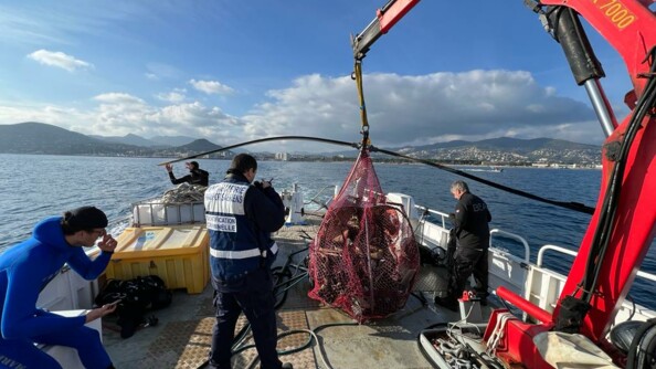 Des gendarmes sur un bateau en mer qui ont répêché une épave d'hélicoptère. Au second plan, le golfe de Cannes