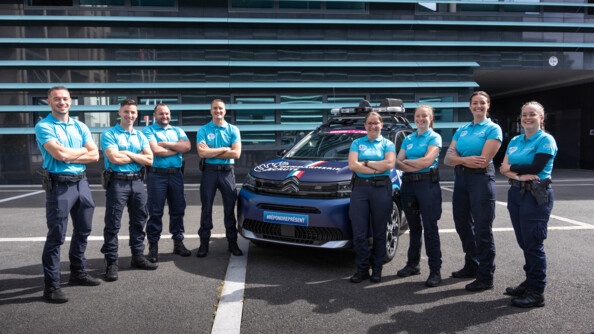 De part et d'autre d'un véhicule gendarmerie du Tour de France, 4 hommes et 4 femmes de la gendarmerie, bras croisés