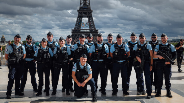 Des gendarmes posent devant et sur la Place du Trocadéro, à Paris. Derrière eux se dresse la tour Eiffel, sur laquelle sont aposés les anneaux des Jeux olympiques et paralympiques.