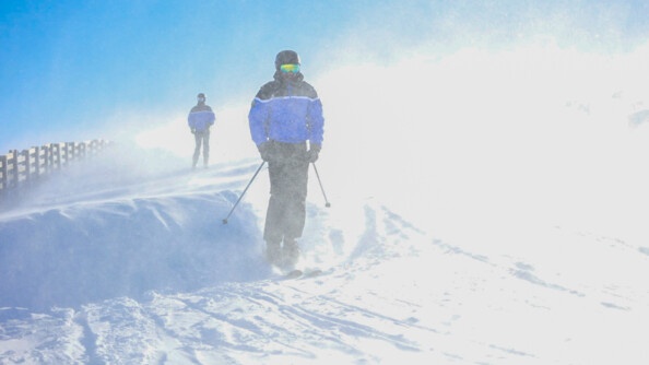 Deux gendarmes en train de skier dans la neige qui vole au vent, en arrière plan, le ciel bleu