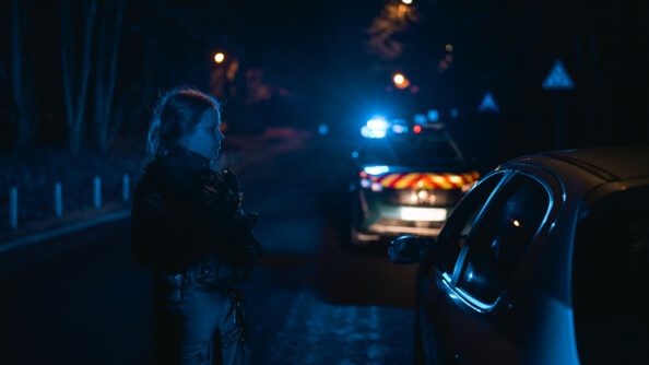 Une gendarme devant une voiture. Il fait nuit et sombre.