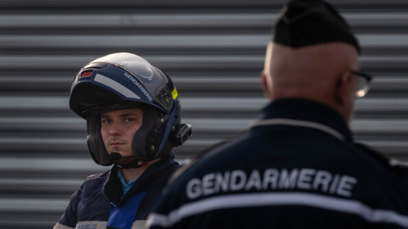 un motard de la gendarmerie en buste avec son casque relevé. Devnat lui, flou, à droite, un autre gendarme