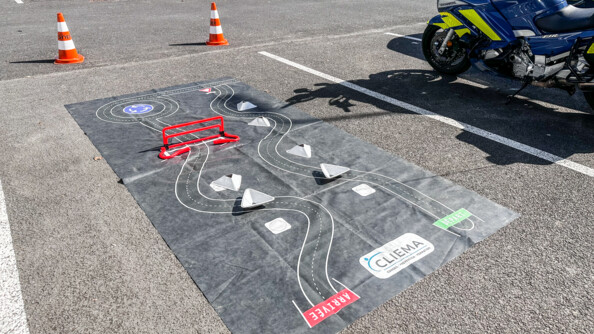 un parcours d'obstable au sol sur un tracé de circuit version sécurité routière, encadrée par des plots. A droite une moto gendarmerie